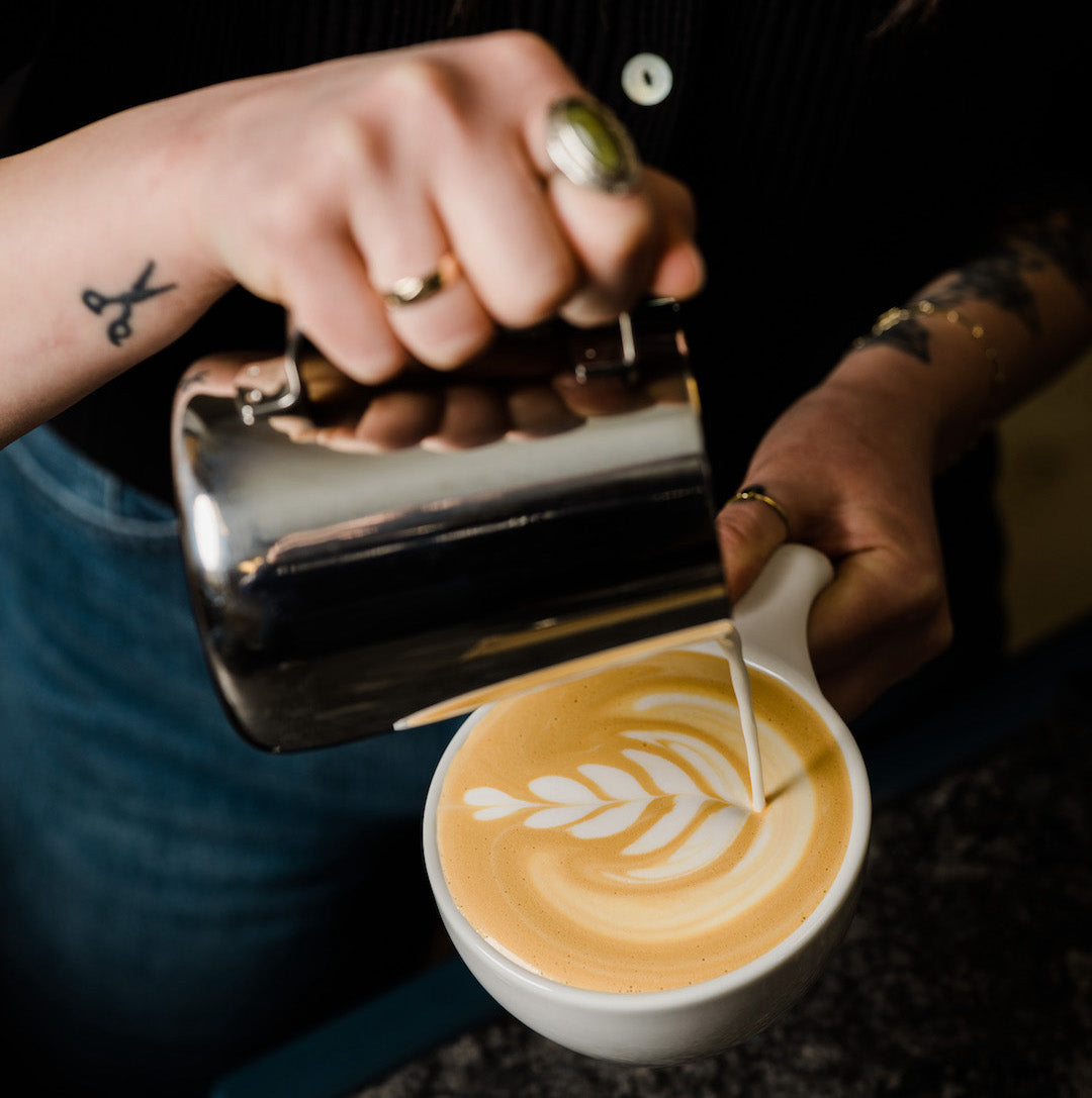 Barista pouring a latte art design with milk.